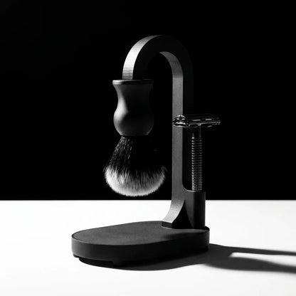 Matte black shaving stand holding a synthetic shaving brush and chrome double-edge safety razor on oval base