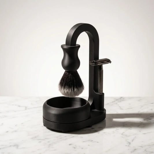 Matte black shaving set with safety razor, shaving brush, and arched stand with bowl on marble surface