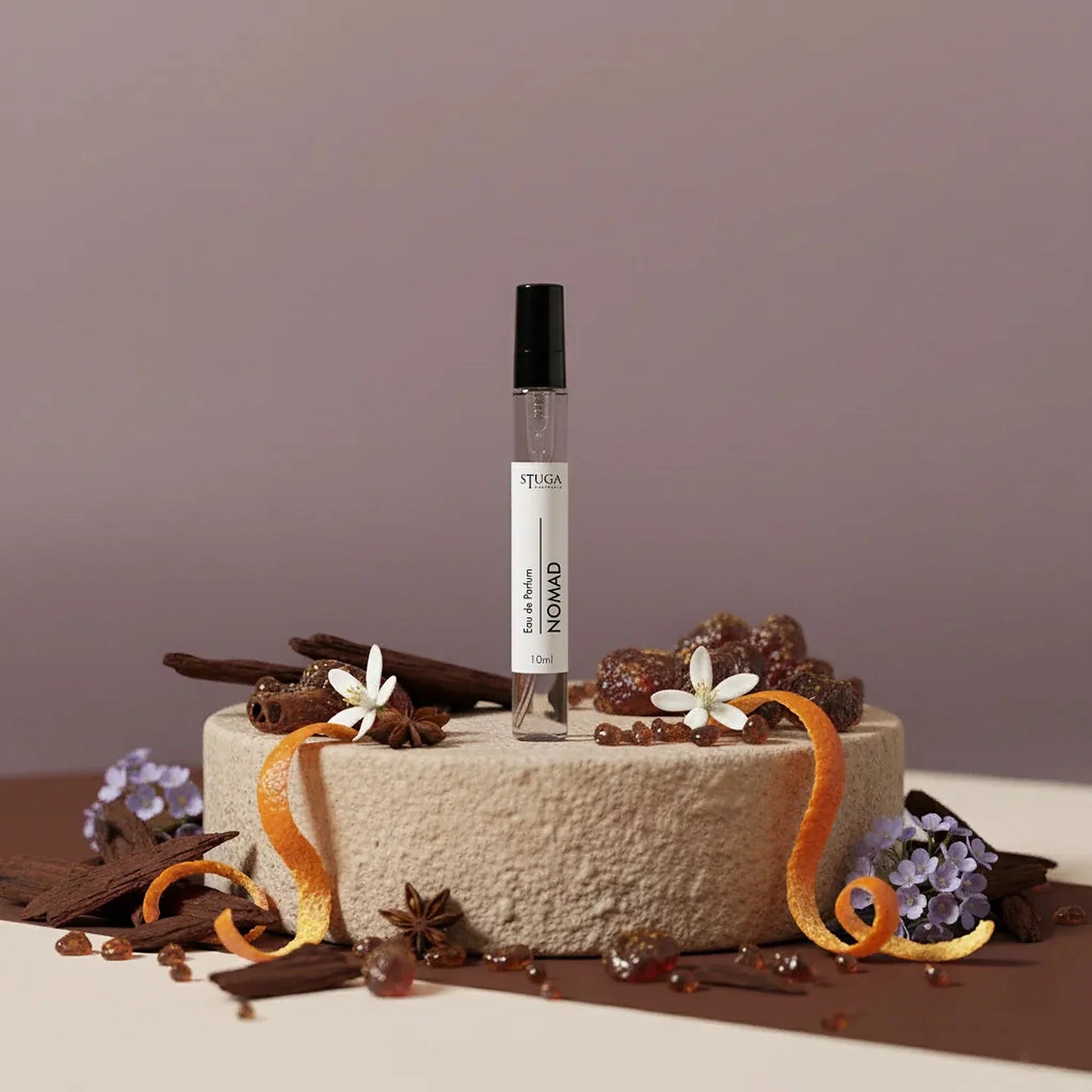 Stuga Nomad 10ml Eau de Parfum spray bottle on a stone pedestal, surrounded by cinnamon sticks, star anise, orange peel, and 