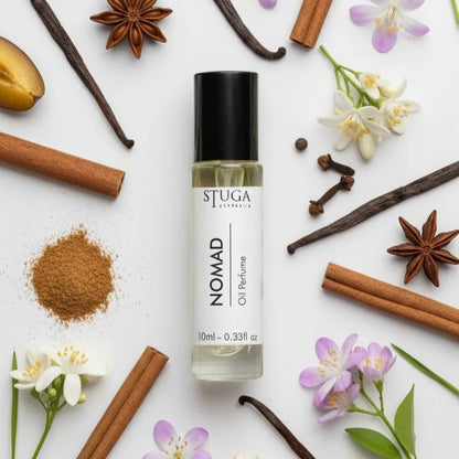 Nomad oil perfume in clear glass bottle with black cap surrounded by cinnamon sticks, vanilla pods, star anise, cloves, and f