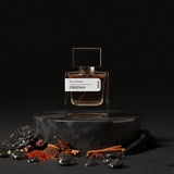 Stuga Obsidian Eau de Parfum 30ml bottle on a dark marble stand, surrounded by spices and dark stones.