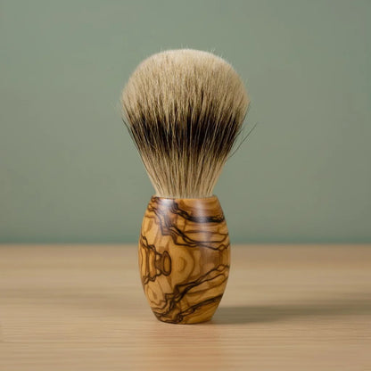 2nd grade badger bristle shaving brush with a beautifully grained olive wood handle, standing on a wooden surface.