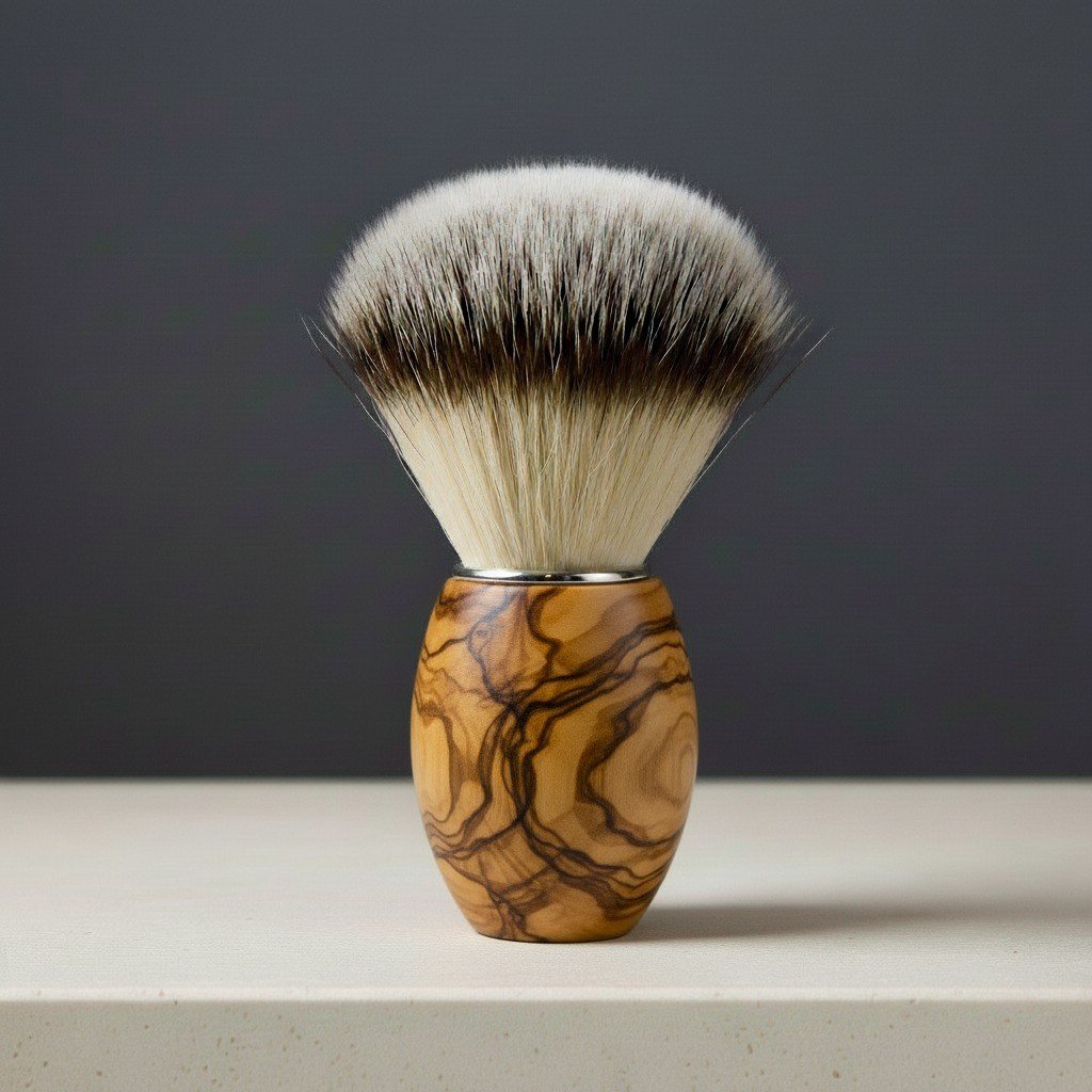 Olive wood shaving brush with synthetic badger-style bristles and a polished metal collar, standing upright on a light surfac
