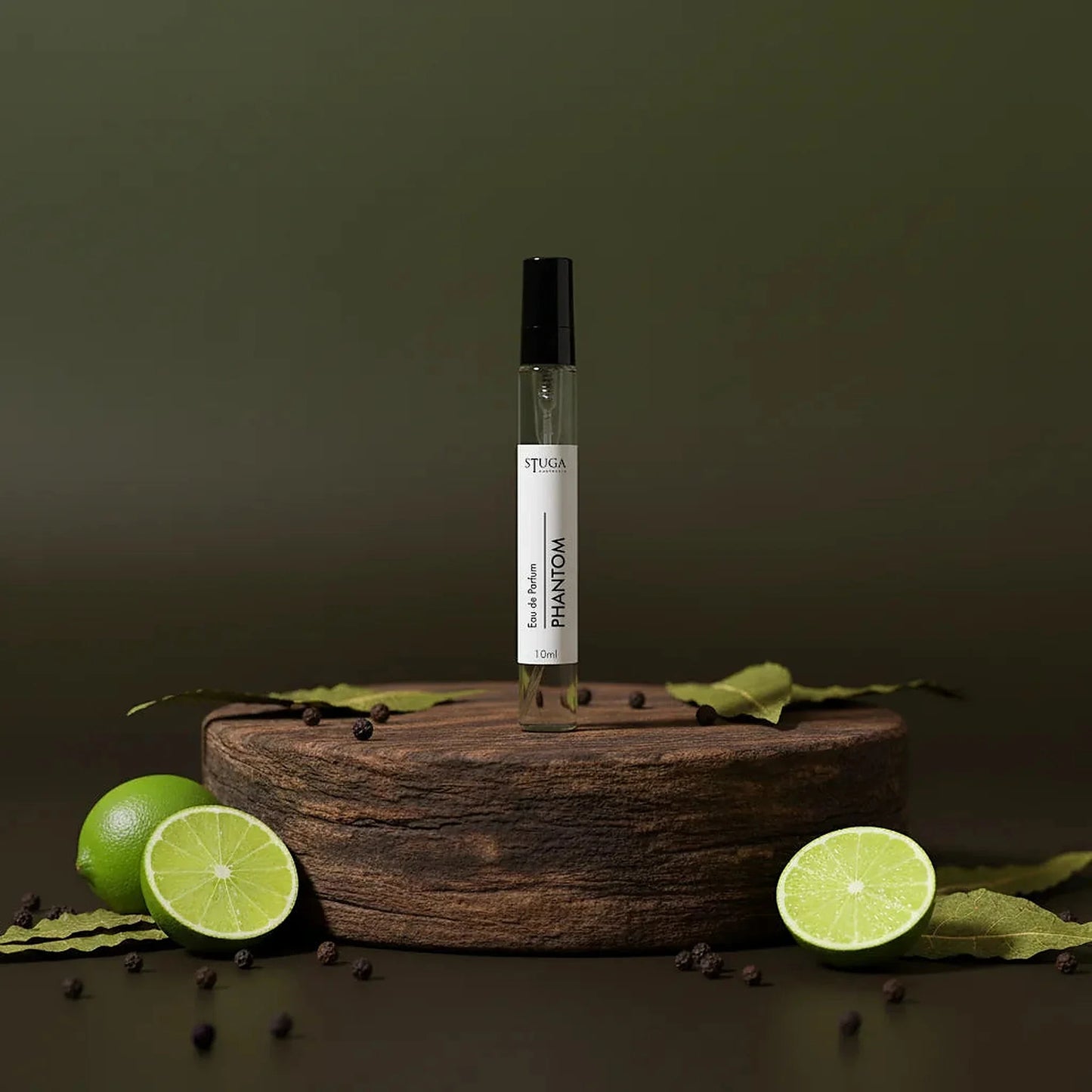 Stuga Phantom Eau de Parfum 10ml spray bottle on a wooden stand with fresh limes and peppercorns.