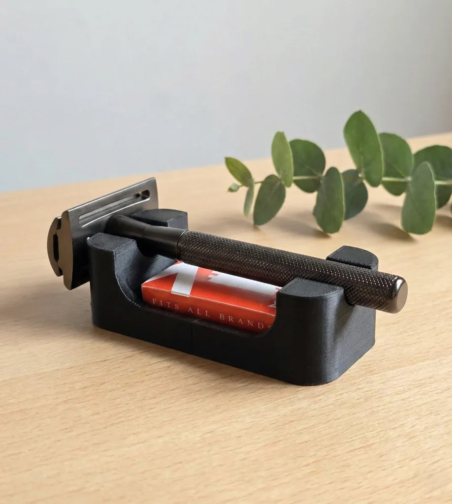 Black safety razor stand with built-in blade storage compartment, holding a dark gunmetal DE razor and blade pack