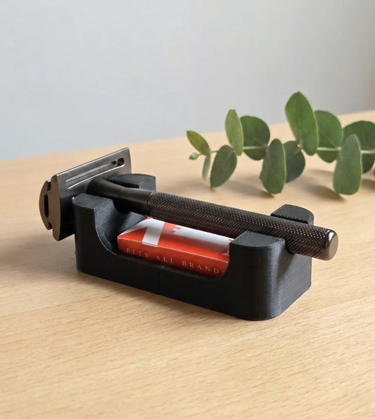Black safety razor stand with built-in blade storage compartment, holding a dark gunmetal DE razor and blade pack