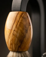 Shaving brush with polished olive wood handle and natural bristles displayed on a dark metal stand