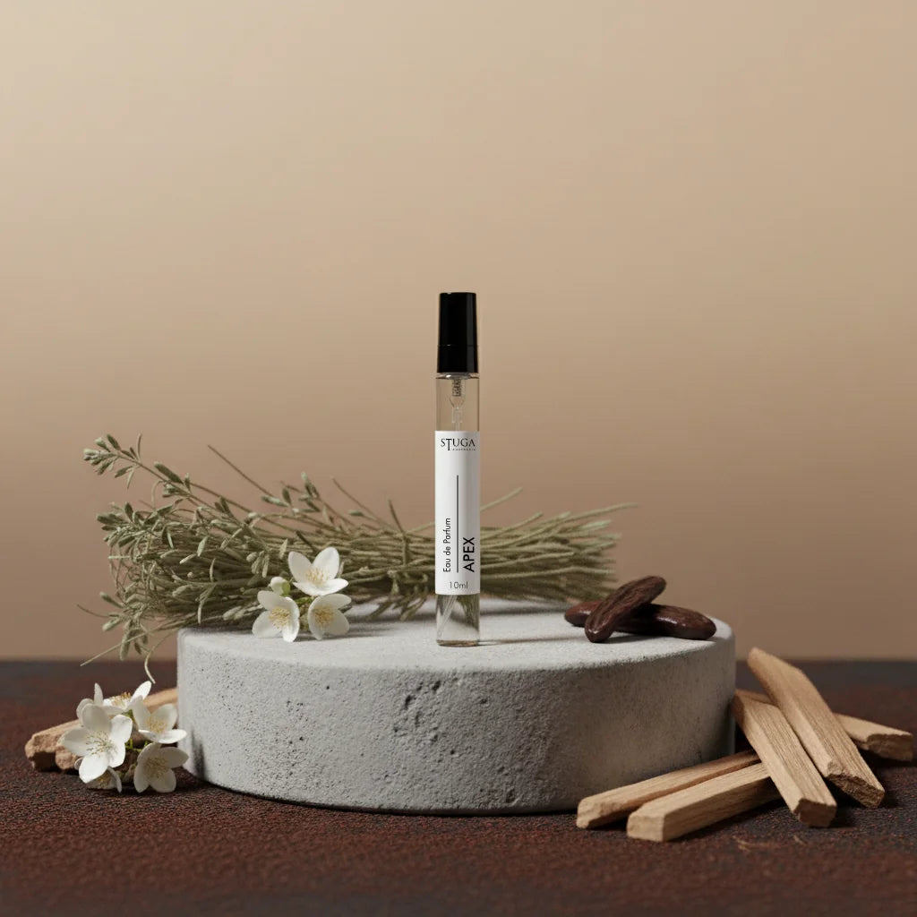 Stuga Apex 10ml Eau de Parfum bottle on a concrete stand with dried herbs, white flowers, and wood chips.