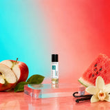 Stuga Apple No. 341 apple oil perfume, 10ml roll-on bottle on a clear acrylic block, with a halved red apple, a slice of watermelon, vanilla pods and a vanilla flower.
