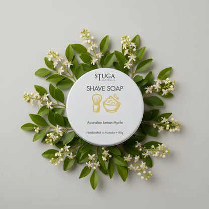 Stuga Australia Australian Lemon Myrtle Shave Soap in a white tin, surrounded by green leaves and small white flowers.