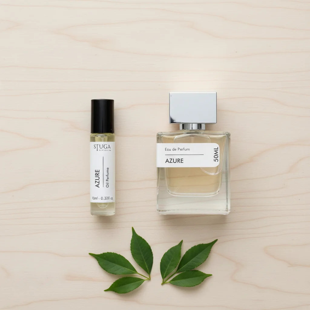 Stuga Azure Eau de Parfum 50ml bottle and 10ml oil perfume rollerball, with green leaves on a light wood background.
