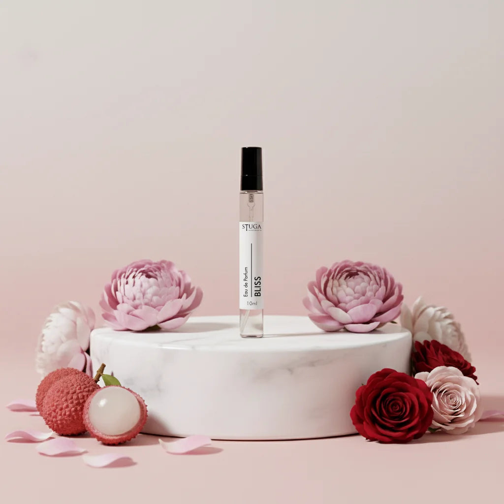 Stuga Bliss Eau de Parfum 10ml rollerball bottle, clear glass with black cap, on a white marble stand surrounded by pink and 