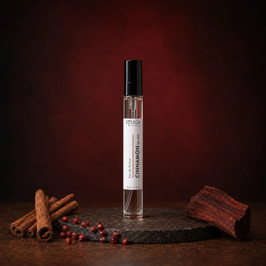 Stuga Cinnamon No. 425 cinnamon perfume, 10ml eau de parfum spray bottle on a dark stone disc with cinnamon sticks, pink peppercorns and mahogany wood against a deep red backdrop.