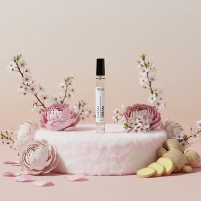 Stuga Dream EDP perfume, 10ml travel size, clear bottle with black cap, surrounded by pink peonies, cherry blossoms, and fres