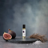 Stuga Fig No. 431 fig oil perfume, 10ml roll-on bottle on a dark green marble plinth with fresh figs, dried grass and sea salt.