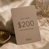 Stuga $200 gift card resting on linen beside a brass bowl and dried flowers