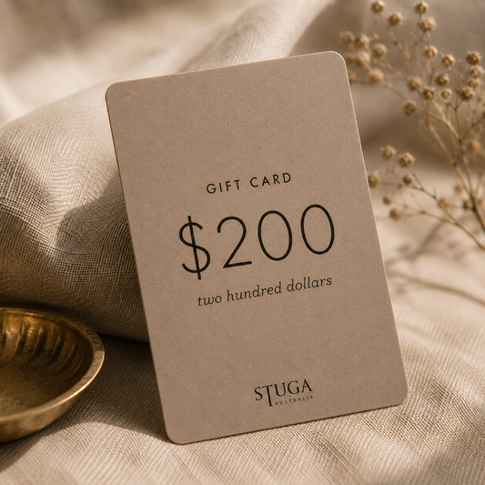 Stuga $200 gift card resting on linen beside a brass bowl and dried flowers