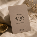 Stuga gift card resting on linen beside a brass bowl and dried flowers