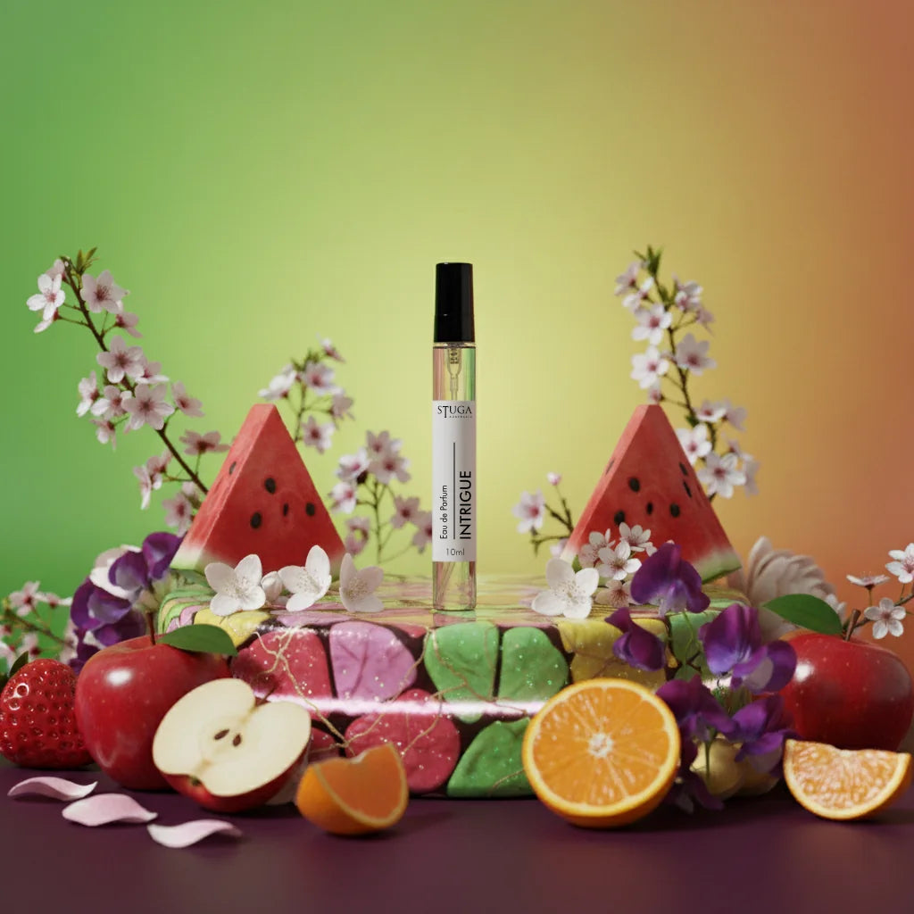 Stuga Intrigue EDP perfume rollerball surrounded by fresh fruit, flowers, and colorful soaps, suggesting a fruity, floral sce