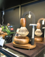 Stuga Magic shaving kit on display, badger brush suspended from the matte black arch over a timber bowl, with a safety razor
