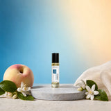 Stuga Neroli No. 437 neroli oil perfume, 10ml roll-on bottle on a grey stone disc, with a ripe peach, orange blossom sprigs and cream silk against a blue and gold background.