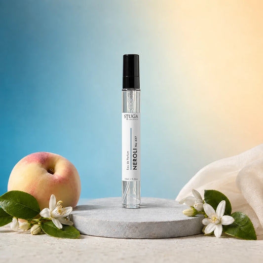 Stuga Neroli No. 437 neroli perfume, 10ml eau de parfum spray bottle on a grey stone disc, with a ripe peach, orange blossom sprigs and cream silk against a blue and gold background.