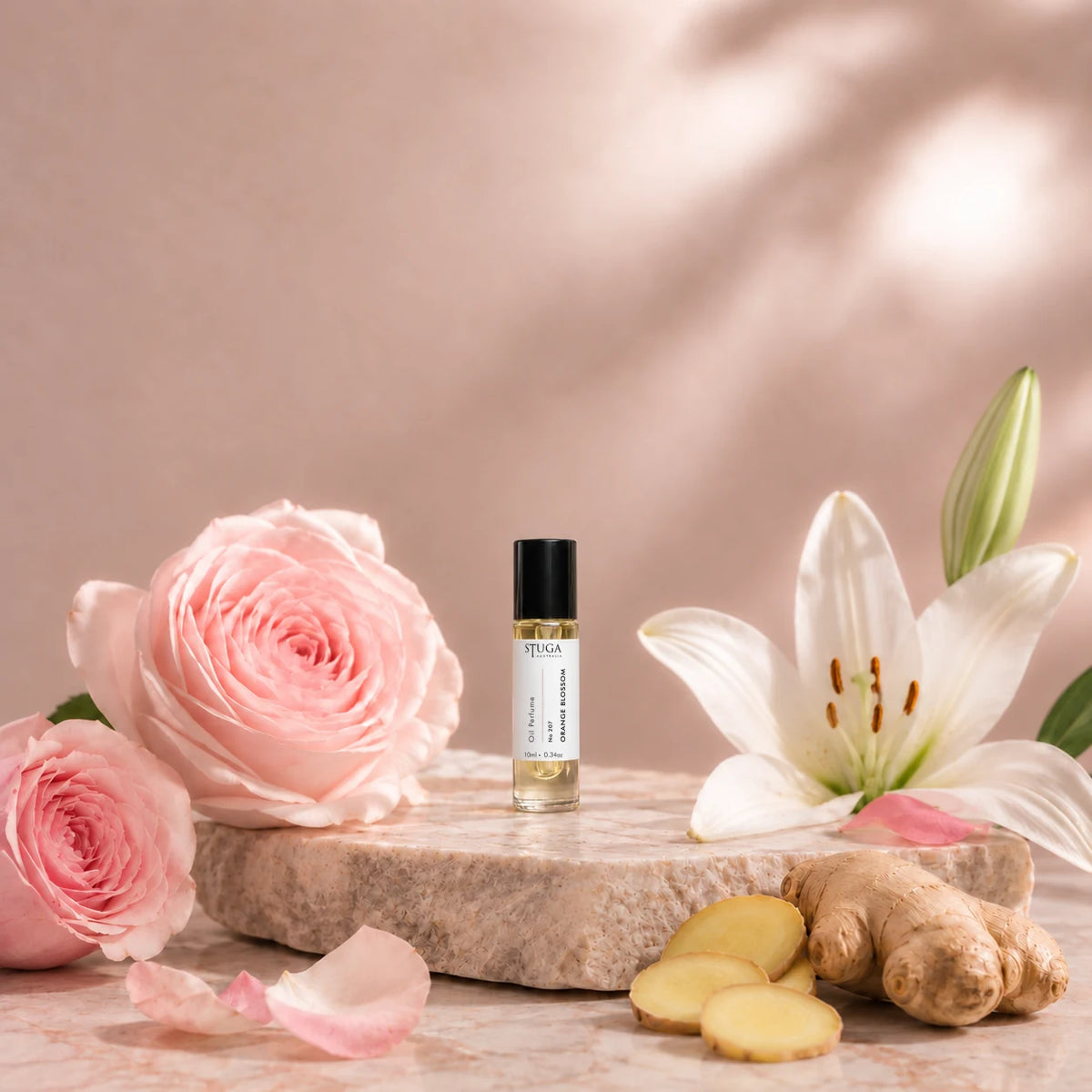 Stuga Orange Blossom No. 207 orange blossom oil perfume, 10ml roll-on bottle on a pale stone slab with pink French roses, a white lily, rose petals and fresh ginger.