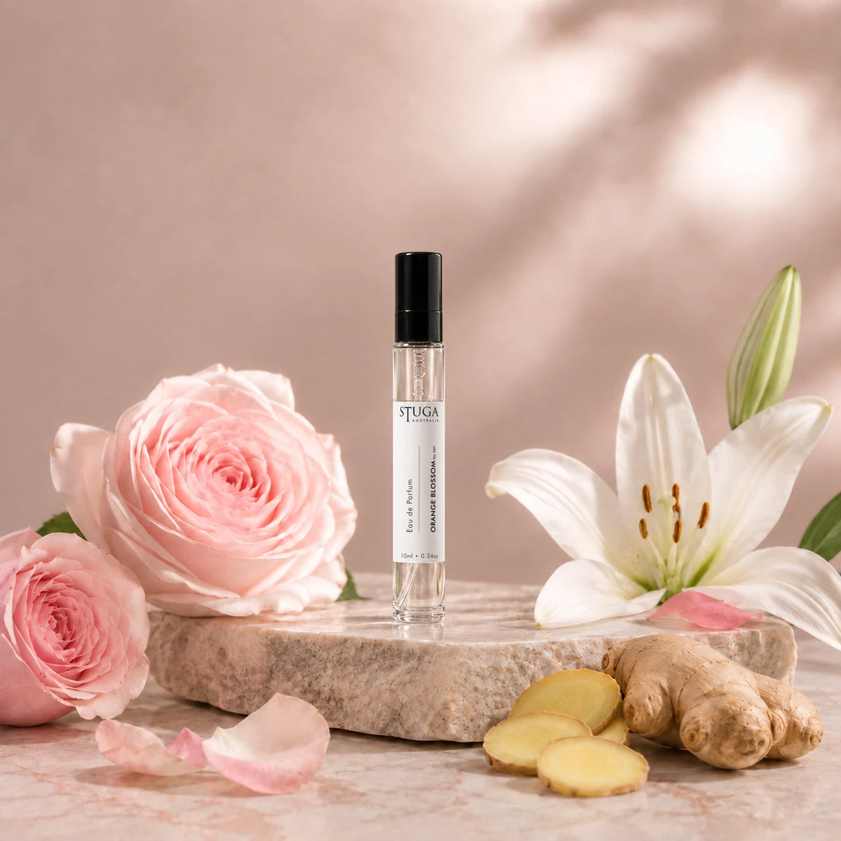 Stuga Orange Blossom No. 207 orange blossom perfume, 10ml eau de parfum spray bottle on a pale stone slab with pink French roses, a white lily, rose petals and fresh ginger.