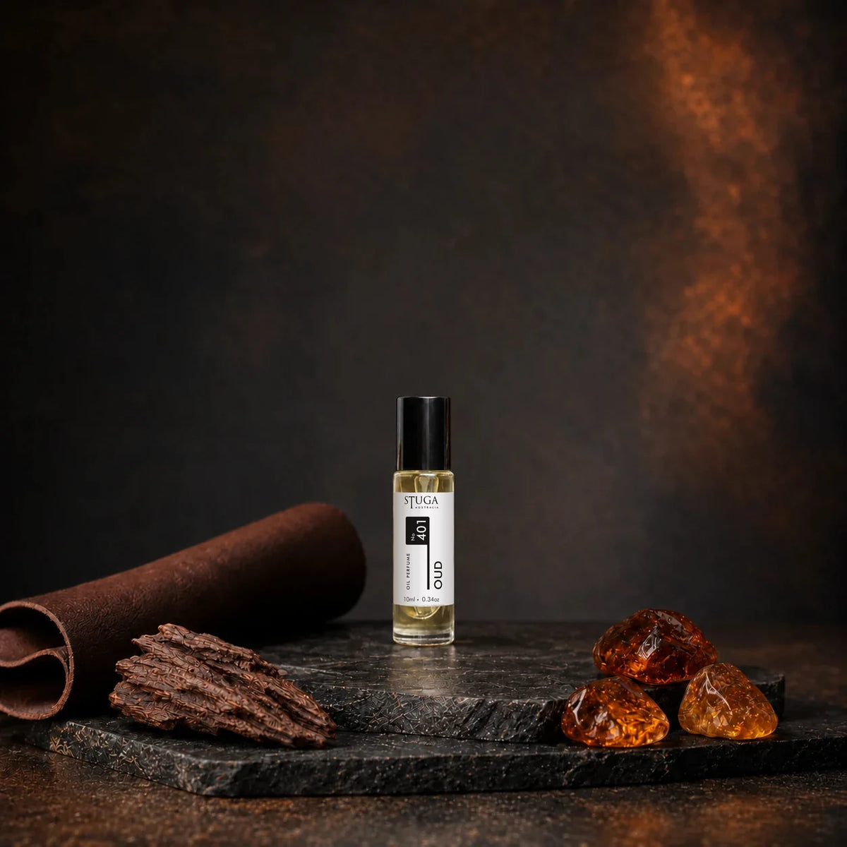 Stuga Oud No. 401 oud oil perfume, 10ml roll-on bottle on dark stone with rolled leather, oud wood chips and golden amber resin.