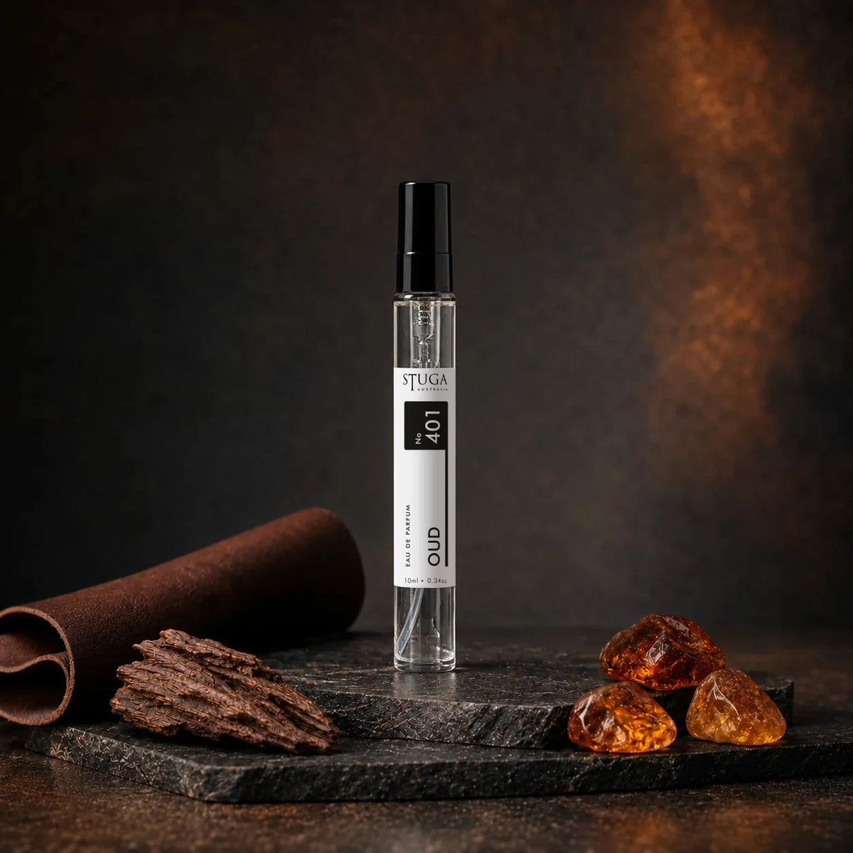 Stuga Oud No. 401 oud perfume, 10ml eau de parfum spray bottle on dark stone with rolled leather, oud wood chips and golden amber resin.