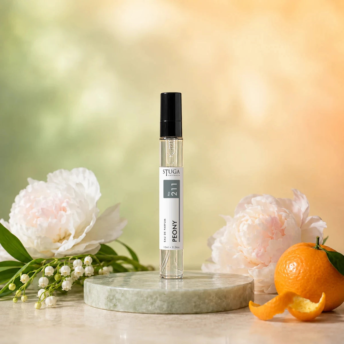 Stuga Peony No. 211 peony perfume, 10ml eau de parfum spray bottle on a pale green marble disc with white peonies, lily of the valley and a mandarin.