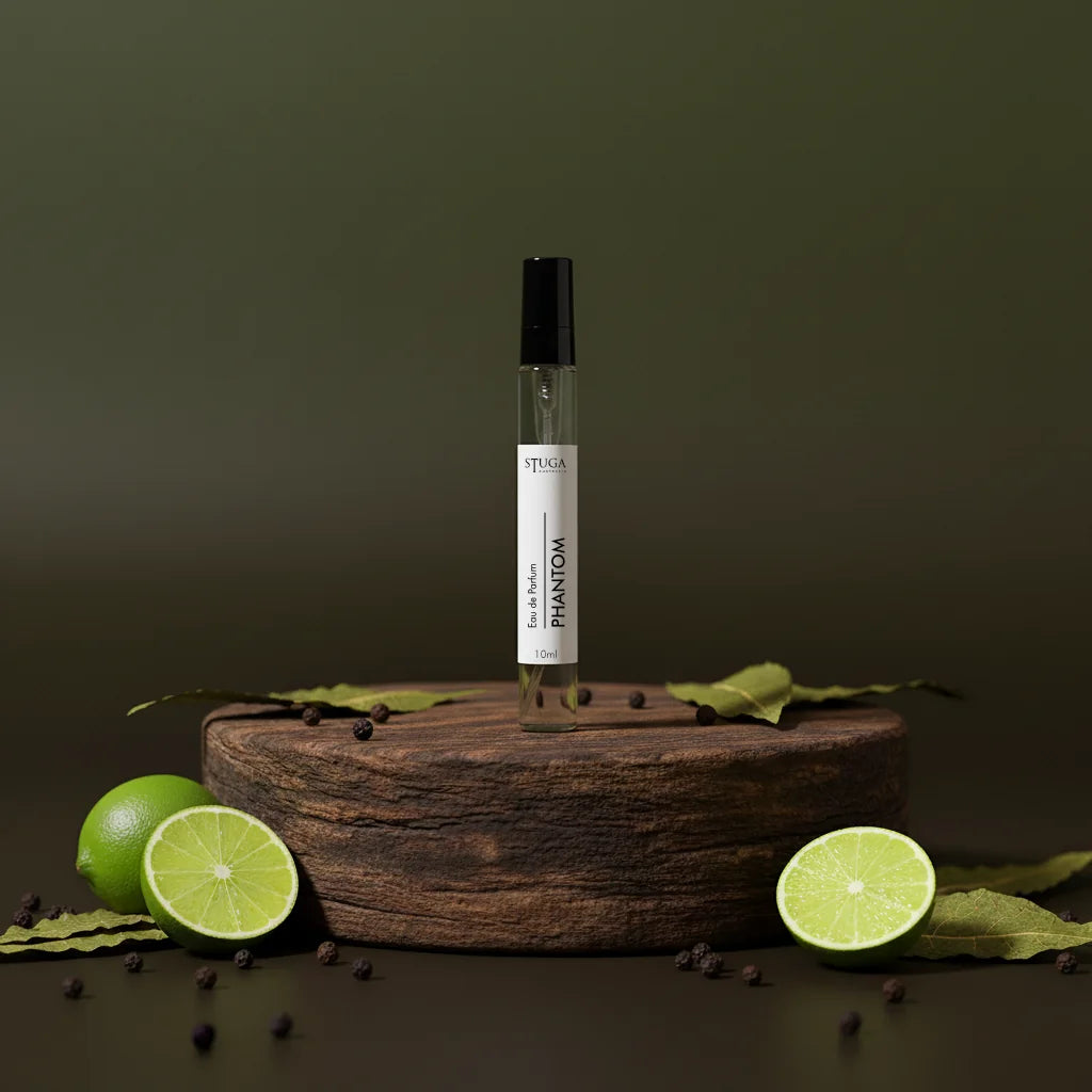 Stuga Phantom Eau de Parfum 10ml spray bottle on a wooden stand with fresh limes and peppercorns.