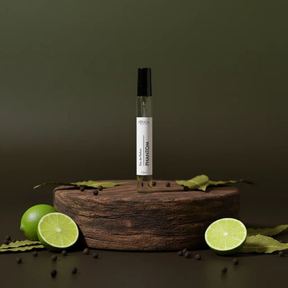 Stuga Phantom Eau de Parfum 10ml spray bottle on a wooden stand with fresh limes and peppercorns.