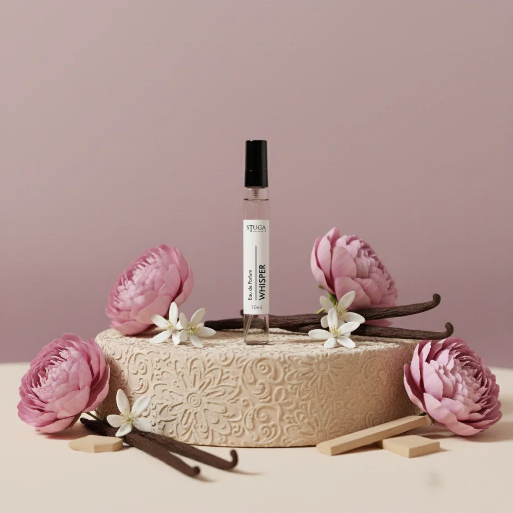 Stuga Whisper 10ml Eau de Parfum with vanilla pods and pink flowers on a textured beige stand.