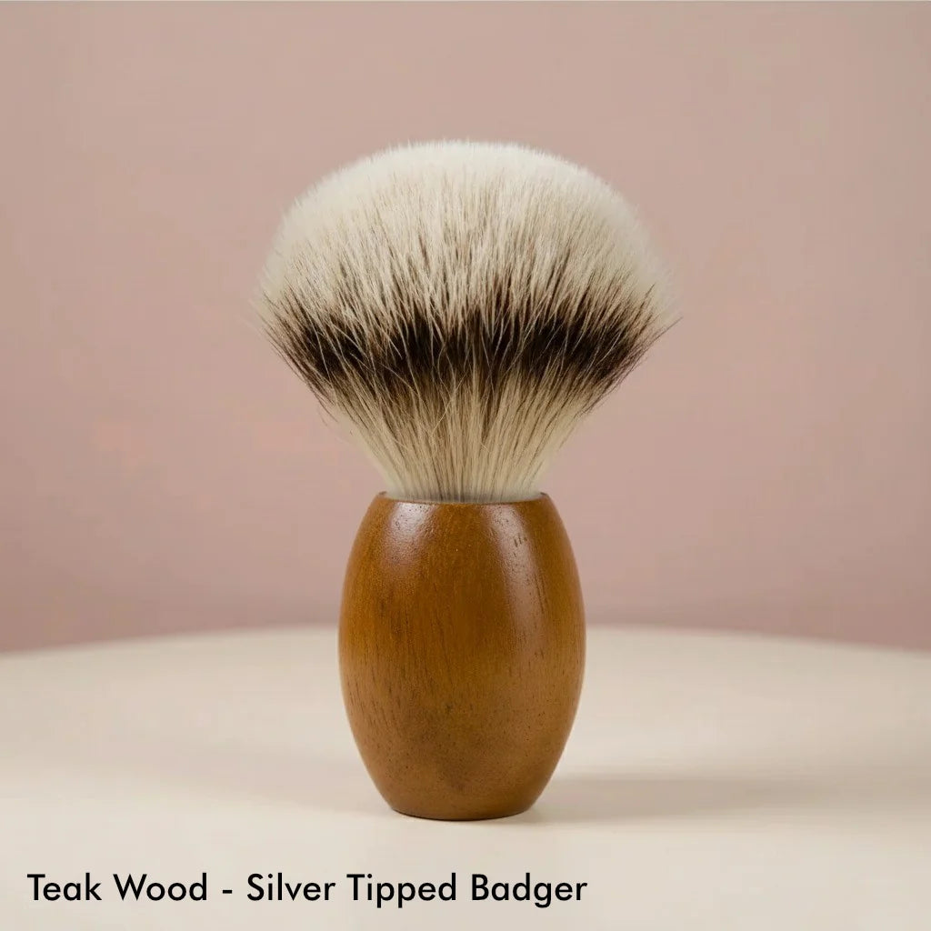 Teak wood handle shaving brush with silver tipped badger bristles on a light background.