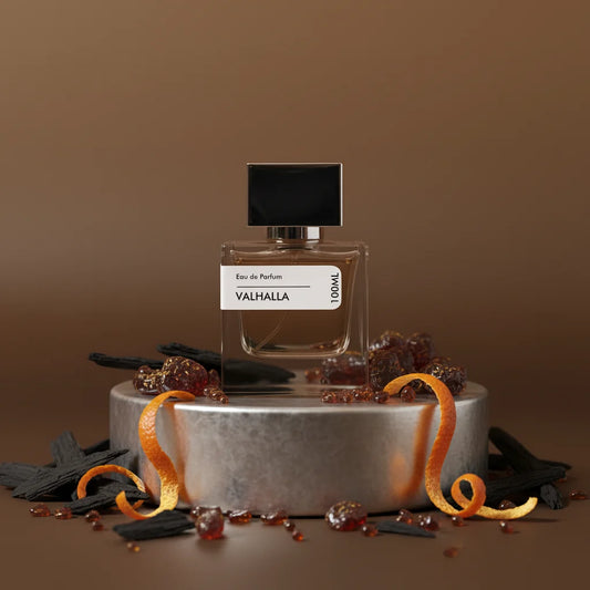 Valhalla Eau de Parfum 100ml bottle with black cap, surrounded by wood chips, amber crystals, and orange peels on a silver pe