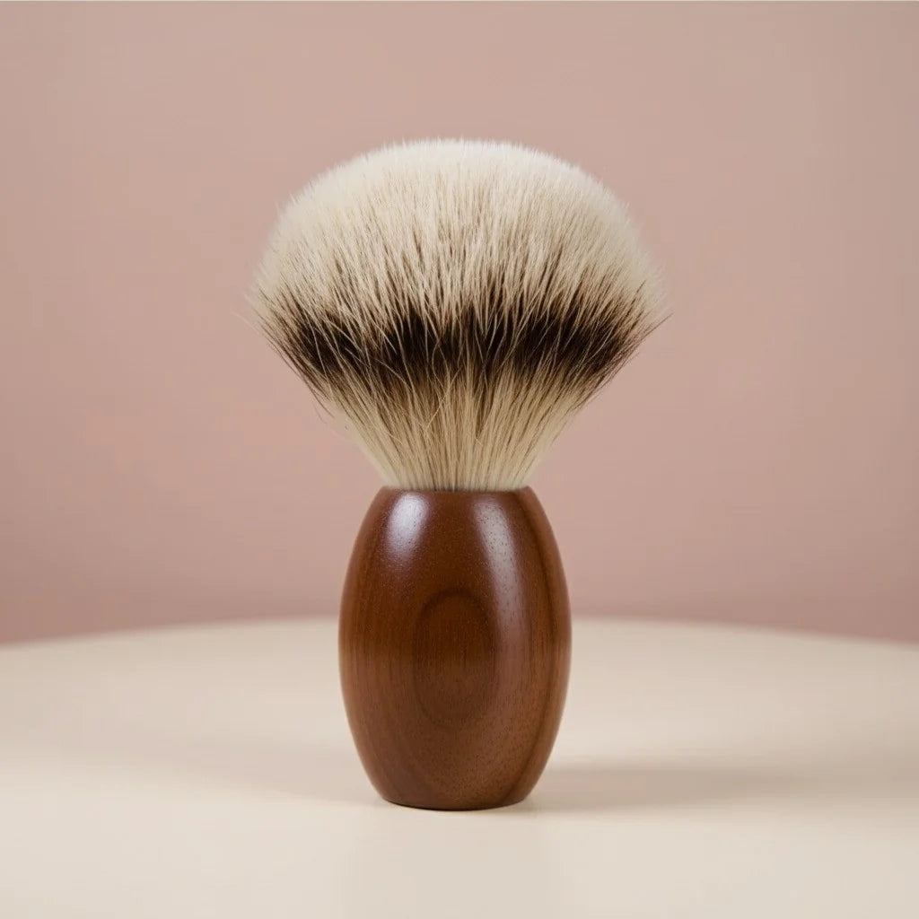 Close-up of a shaving brush with a dark walnut wood handle and soft, silver-tipped badger bristles, set against a light pink 