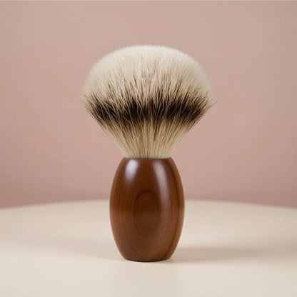 Close-up of a shaving brush with a dark walnut wood handle and soft, silver-tipped badger bristles, set against a light pink 