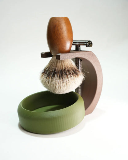 Shaving brush with wooden handle on a brown metal stand next to a green shaving soap bowl for traditional wet shaving