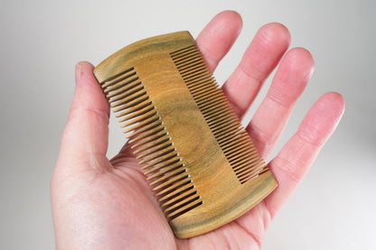 Hand holding a small wooden double-sided comb with fine and wide teeth for hair grooming