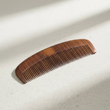 Wooden hair comb in natural hardwood with curved spine on light stone surface