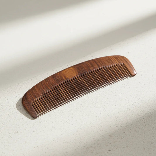 Wooden hair comb in natural hardwood with curved spine on light stone surface