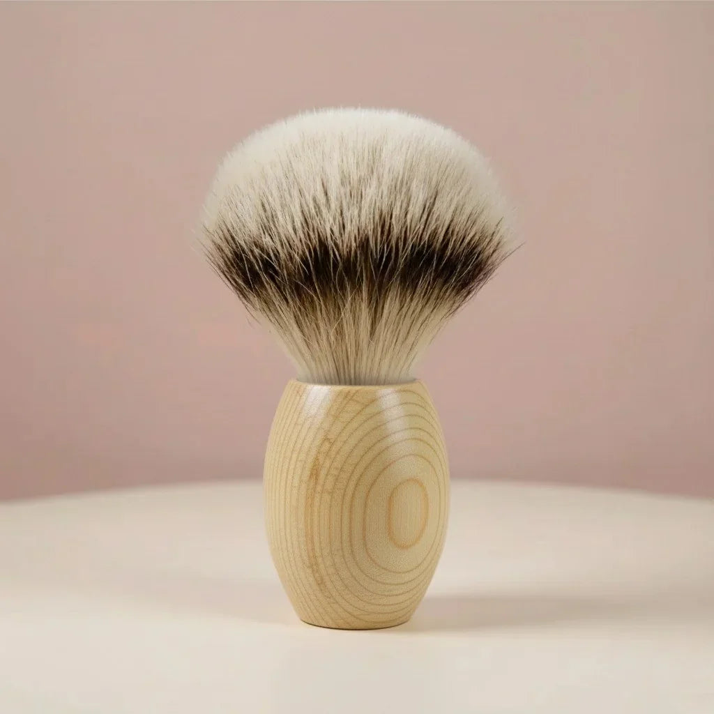 Shaving brush with a light wooden handle and soft, black and white badger hair bristles, ideal for lathering.